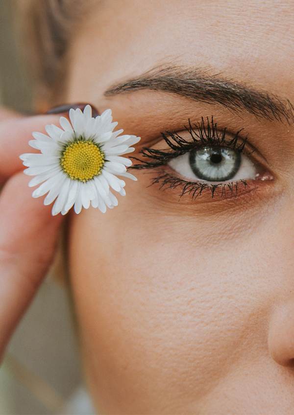 A woman holds a daisy next to her eye