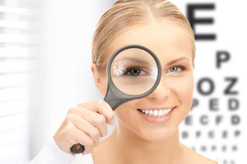 Junge Frau mit Lupe vor einer Optikertafel