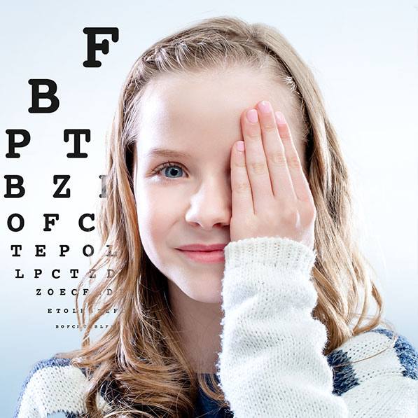 Ein junges Mädchen mit Hand vor einem Auge vor Buchstabentafel