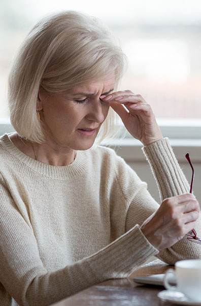 An older woman with office eye syndrome rubs her eye